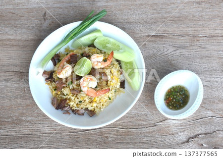 fried rice shrimp topping piece of beef meat and egg with slice cucumber couple lemon on plate dressing chili fish sauce cup 137377565