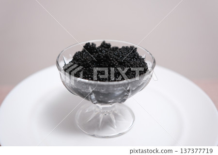Glass bowl and spoon with black caviar on white background Salted black caviar in a metal dish on a dark stone background. Selective focus. Glass bowl and spoon with black caviar on white background Salted black caviar in a metal dish on a dark stone background. Selective focus. 137377719