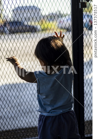 Little One Stares Beyond Front Door, A lone toddler gazing beyond a closed gate, reflecting the overlooked reality of unsupervised children and raising awareness of child safety in society. 137378517