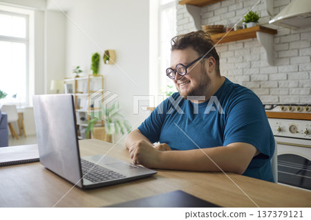 Happy overweight man looking on laptop screen with smile, sitting at table Happy overweight man looking on laptop screen with smile, sitting at table 137379121