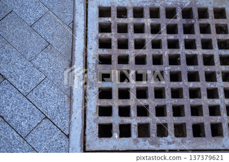 Iron storm drain grate on a granite tiled sidewalk for rain water collection Iron storm drain grate on a granite tiled sidewalk for rain water collection 137379621