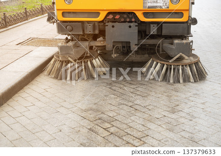 Modern street cleaning vehicle with rotating brushes working in an urban area Modern street cleaning vehicle with rotating brushes working in an urban area 137379633
