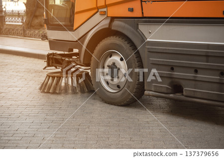Green municipal cleaning vehicle sweeping a city street during the morning. Green municipal cleaning vehicle sweeping a city street during the morning. 137379656