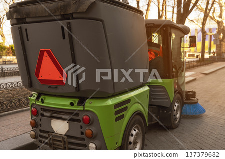 Rear view of a green street cleaning vehicle driving along a city sidewalk 137379682