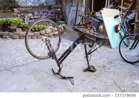 Old bicycle frame turned upside down for maintenance and repair in a city courtyard Old bicycle frame turned upside down for maintenance and repair in a city courtyard 137379699