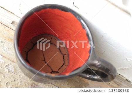 Red and black ceramic coffee cup with coffee grounds. 137380588