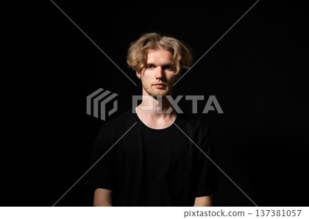 Young blonde man in a low-key studio, serious direct gaze and confident posture conveying individuality, contemporary fashion and modern lifestyle in a dramatic portrait Young blonde man in a low-key studio, serious direct gaze and confident posture conveying individuality, contemporary fashion and modern lifestyle in a dramatic portrait 137381057