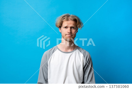 Young man having doubts and feeling uncertain, standing with a skeptical facial expression indicating hesitation, frustration, and disappointment Young man having doubts and feeling uncertain, standing with a skeptical facial expression indicating hesitation, frustration, and disappointment 137381060