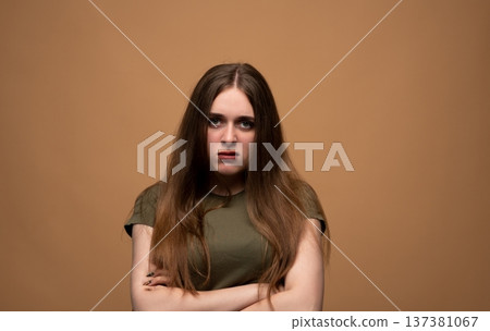 Young woman standing displeased, expressing anger and annoyance with crossed arms against a solid background Young woman standing displeased, expressing anger and annoyance with crossed arms against a solid background 137381067