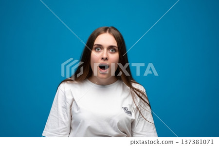 Young woman having surprised, shocked, or amazed expression on blue background, showing emotion, wonder Young woman having surprised, shocked, or amazed expression on blue background, showing emotion, wonder 137381071