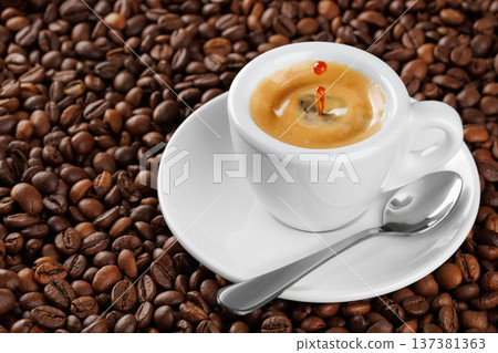 Small white espresso cup with splash and drop, brimming with aromatic coffee resting on bed of roasted beans 137381363