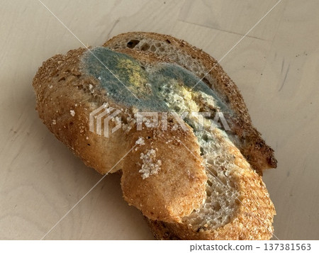Moldy slice of bread with visible green and yellow discoloration on wooden surface 137381563