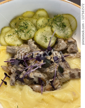 Mashed potatoes with creamy mushroom sauce topped with greens, served with sliced cucumbers Mashed potatoes with creamy mushroom sauce topped with greens, served with sliced cucumbers 137381572