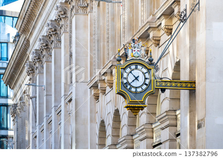 A street clock hangs on the Bank building in the City of London. The clock shows the time and adds character to the historic architecture. People walk by in this busy area of the city. A street clock hangs on the Bank building in the City of London. The clock shows the time and adds character to the historic architecture. People walk by in this busy area of the city. 137382796