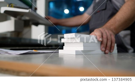 Industrial worker operating a production machine and stacking white panels on a workshop table. Industrial worker operating a production machine and stacking white panels on a workshop table. 137384905