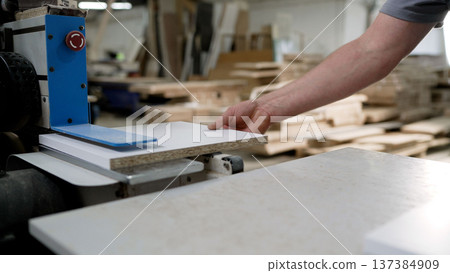 Worker processing a laminated particle board panel on industrial machinery in a furniture workshop. Worker processing a laminated particle board panel on industrial machinery in a furniture workshop. 137384909