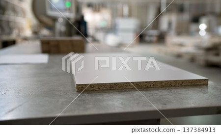 White laminated chipboard panel on a worktable in a furniture manufacturing workshop with blurred background. 137384913