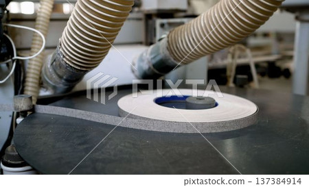 Roll of edge banding on an industrial woodworking machine in a furniture production workshop. 137384914