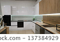 Modern kitchen design with glossy white cabinets, wood accents, and built-in appliances in a showroom 137384929