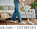 Woman in jeans using cordless vacuum cleaner on living room floor near sofa 137385163