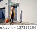 Woman with suitcase walking out of modern building in sunlight 137385164