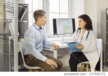 Doctor holding clipboard talks with male patient in bright clinic office 137385172