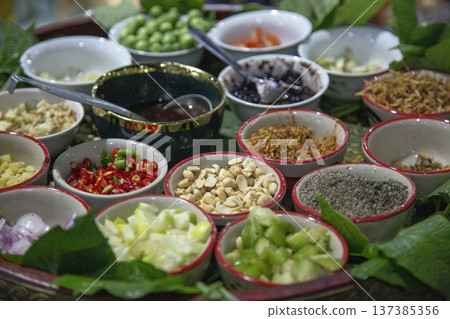 Traditional Thai appetizer Miang Kham set with various herbal ingredients like chili, lime, peanuts, and ginger served in small bowls on betel leaves for a healthy snack Traditional Thai appetizer Miang Kham set with various herbal ingredients like chili, lime, peanuts, and ginger served in small bowls on betel leaves for a healthy snack 137385356