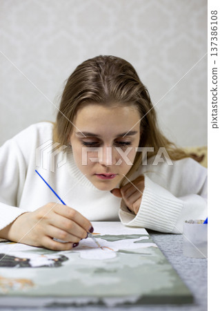 Girl carefully applies paint to her drawing. Precise work requiring concentration. Professional young artist prepares her painting for exhibition. The process of creating masterpiece 137386108