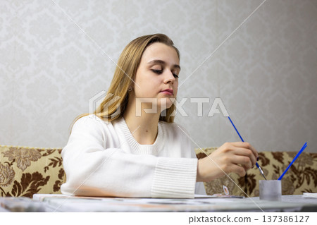 Blonde girl learns to hold brush and use it to paint picture. Woman decided to learn to paint as an adult. Desire to master new hobby. Attempt to paint her first picture 137386127