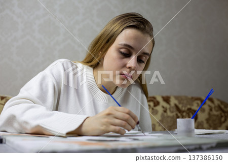 Young female self taught artist is trying to figure out how to paint. Incorrect painting technique due to lack of skill. Self teaching how to hold brush and apply paint to painting Young female self taught artist is trying to figure out how to paint. Incorrect painting technique due to lack of skill. Self teaching how to hold brush and apply paint to painting 137386150