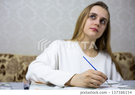 Girl hand with brush paints picture, while head points upward with blurred background. Process of understanding one painting and creative inspiration. Finding ideas for drawing and creativity 137386154