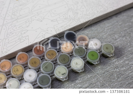 Colorful paint pots arranged neatly beside painting grid. Calm, creative atmosphere. Artistic process invites quiet focus and imagination. Ideal for tutorials, crafting blogs Colorful paint pots arranged neatly beside painting grid. Calm, creative atmosphere. Artistic process invites quiet focus and imagination. Ideal for tutorials, crafting blogs 137386181