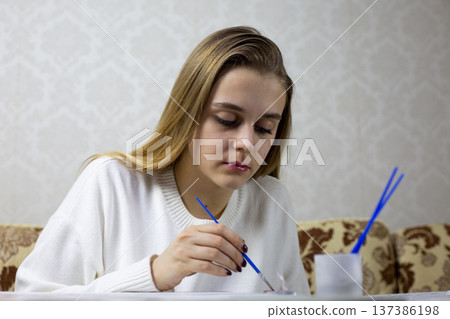 The process of painting picture. Girl hand dips brush into paint to transfer it to canvas. Moment of concentration while creating drawing The process of painting picture. Girl hand dips brush into paint to transfer it to canvas. Moment of concentration while creating drawing 137386198