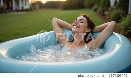 A woman relaxing in a blue inflatable tub filled with ice, set in a green outdoor lawn, enjoying a refreshing moment of wellness. Inflatable Ice Bath Concept For Home 137386402
