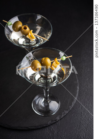 Two glasses with elegant cocktail martini with skewered green olives and a lemon twist on dark textured background Two glasses with elegant cocktail martini with skewered green olives and a lemon twist on dark textured background 137386490