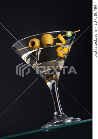 Classic Martini with Olives and Lemon Twist on Dark Background. Elegant Cocktail Composition Classic Martini with Olives and Lemon Twist on Dark Background. Elegant Cocktail Composition 137386494