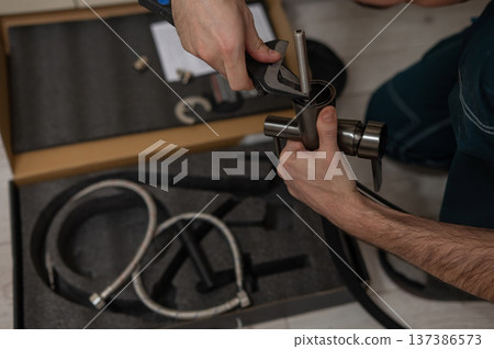 A plumber is replacing a faucet in the kitchen. A plumber is replacing a faucet in the kitchen. 137386573