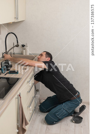 A plumber is replacing a faucet in the kitchen. A plumber is replacing a faucet in the kitchen. 137386575