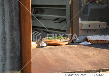 Fresh pizza, wooden serving board at restaurant pickup window, prepared meal waiting for customer near kitchen counter, pizza boxes. Food service, restaurant takeaway, fast casual dining, hospitality Fresh pizza, wooden serving board at restaurant pickup window, prepared meal waiting for customer near kitchen counter, pizza boxes. Food service, restaurant takeaway, fast casual dining, hospitality 137386658