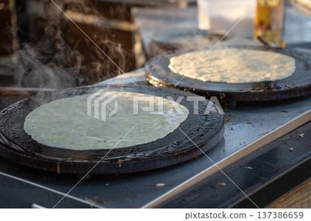 Thin pancakes cooking on round griddle plates with steam rising from hot surface, traditional crepe preparation during Maslenitsa celebration, outdoor food stall. Traditional festival food 137386659