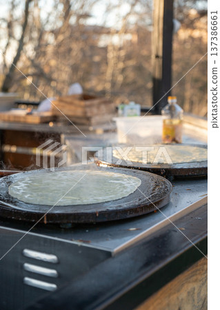 Thin pancakes cooking on round griddle plates with steam rising from hot surface, traditional crepe preparation during Maslenitsa celebration, outdoor food stall. Traditional festival food 137386661