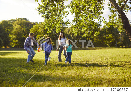 Active children and their parents playing football in park, moving and laughing Active children and their parents playing football in park, moving and laughing 137386887