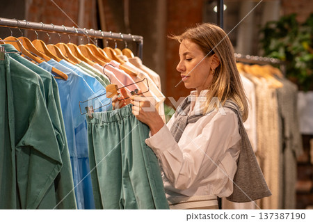 Positive woman customer shopping in clothing store, buying fashionable outfit in fashion showroom. 137387190