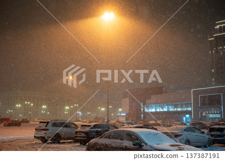 Heavy winter snowfall and blizzard in city, parking lot with cars near supermarket covered in snow. 137387191