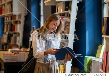 Intelligent woman booklover reading book in cozy bookshop, flipping through pages of publication. 137387201