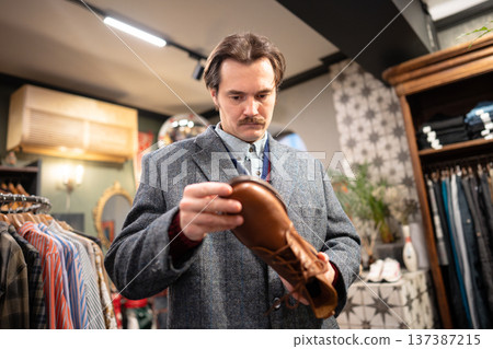 Serious handsome man customer thinking on buying fancy leather shoes in second hand vintage shop. 137387215