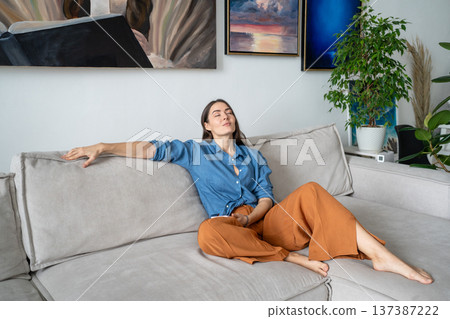 Dreamy tranquil woman artist sits on couch at home gallery apartment, thinking about artwork ideas. Dreamy tranquil woman artist sits on couch at home gallery apartment, thinking about artwork ideas. 137387222