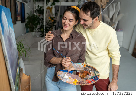Loving couple of artists enjoys finished painting, partners pleased with result and share happiness. 137387225