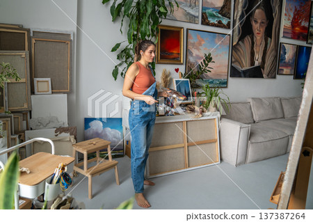 Focused painter woman looking at painting on easel in cozy modern loft studio, art hobby therapy. 137387264