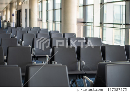Interior of airport terminal with empty seats in a row in departure area of airport without people Interior of airport terminal with empty seats in a row in departure area of airport without people 137387275